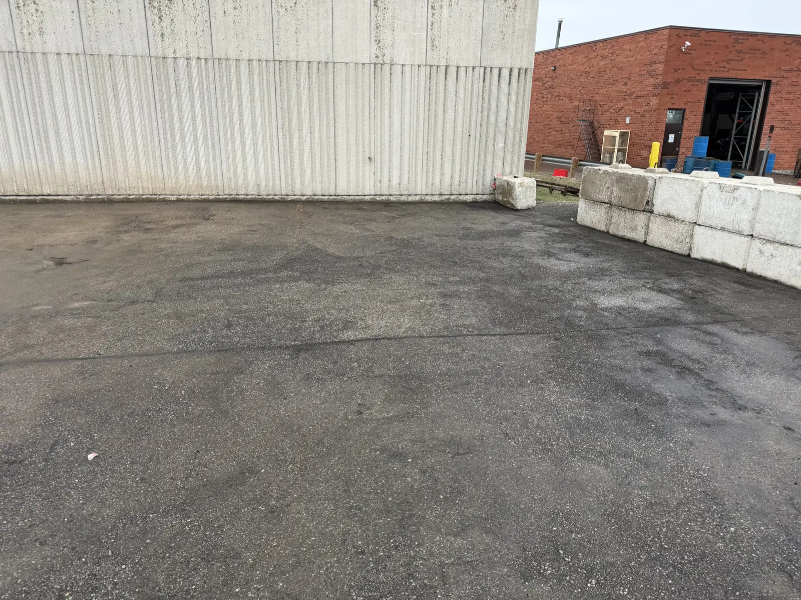 Commercial yard in Mississauga mid pressure washing job, washed pavement beside asphalt still dark with grime