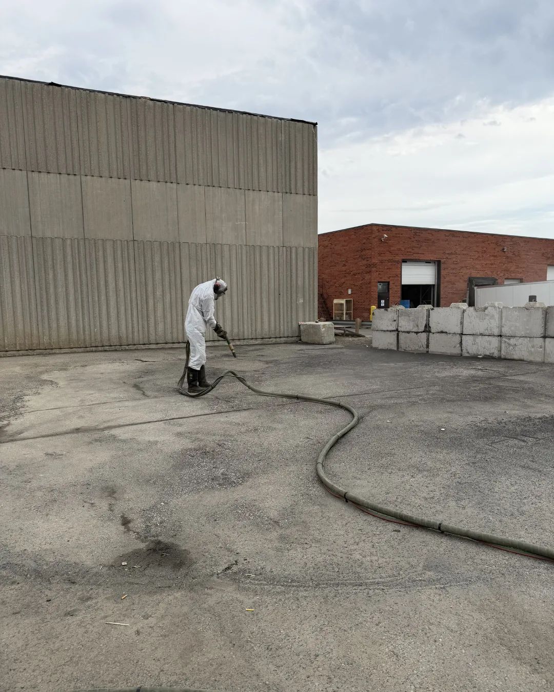 Technician in a protective suit dustless sandblasting a concrete panel wall at a GTA industrial site