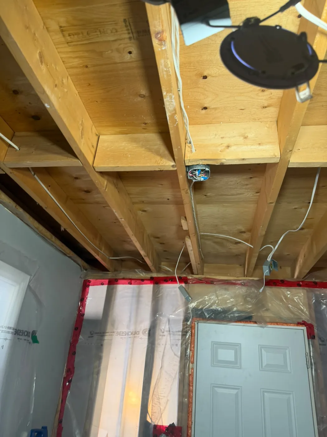 Ceiling joists cleaned back to bare wood by dry ice blasting, with sealed poly-covered walls below ready for rebuild