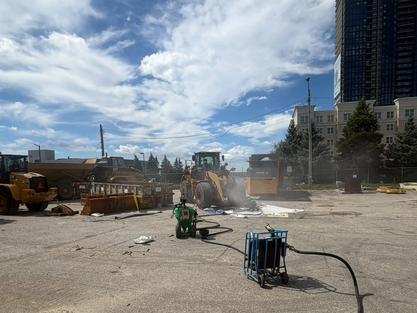 Pure Blast Solutions blast pot and water tank set up on an active GTA contractor yard, blasting a wheel loader with a condo tower directly behind the fence