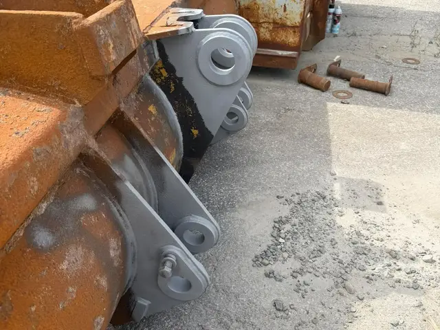 Excavator bucket at a GTA contractor yard with its pin lugs sandblasted back to clean metal while the rest of the bucket is still rusted