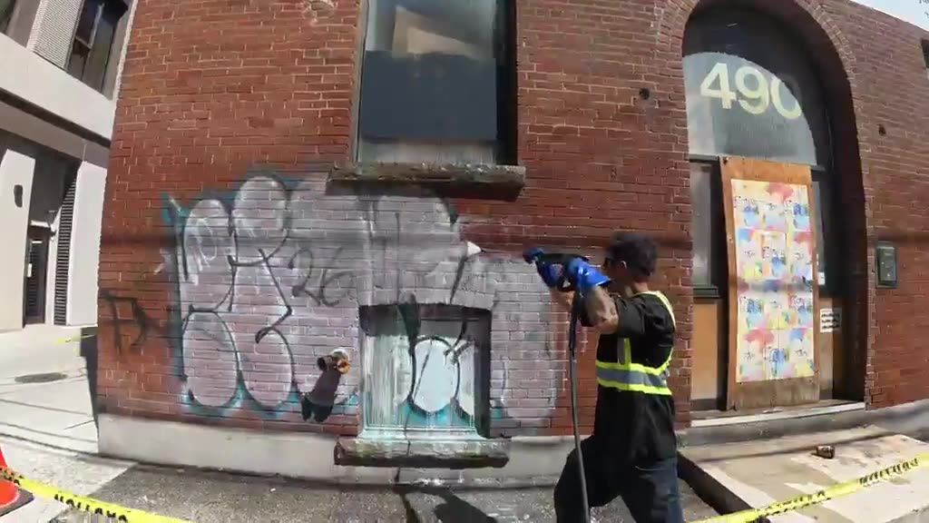 Pressure washing graffiti off a brick storefront in Toronto